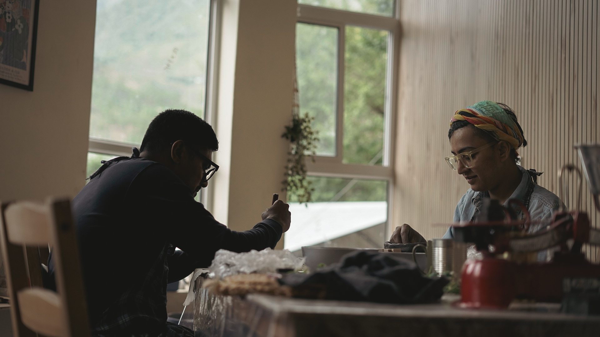 Two makers hand-building at the communal table with a mountain view